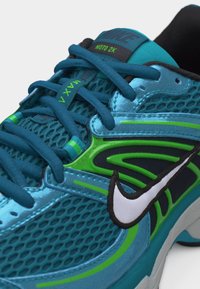 Μπλε αθλητικό παπούτσι Nike Moto 2K με πράσινες λεπτομέρειες, μαύρο και λευκό λογότυπο Nike, και σκούρες μπλε κορδόνια. Λεπτομέρειες από δίχτυ και συνθετικό υλικό στο πάνω μέρος.