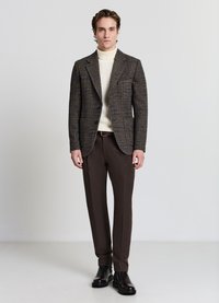 Blazer a quadri marrone con ampi risvolti, indossato sopra un dolcevita a coste crema, abbinato a pantaloni marroni strutturati e stivaletti neri alla caviglia.