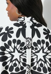 Camicia a righe bianco e nero con motivi floreali e a stelle, caratterizzata da una trama di tessuto liscia e dettagli di piega posteriore.