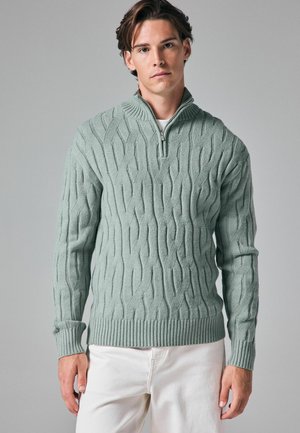 Pulover tricotat de culoare verde deschis, cu guler înalt, fermoar pe jumătate și model texturat cu cabluri. Mânici și tiv cu model dublu.