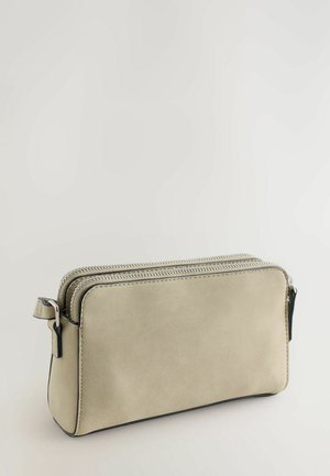 Beežika värvi ristkülikukujuline väike kott kahe hõbedase tõmblukuga tasku ja külje küljes oleva sangaga, asetatud neutraalse hele tausta peale.