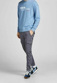 Ljusblå sweatshirt med "core sports" grafik. Grå cargobyxor med fickor. Svarta och blå sneakers med vita snören och sula.