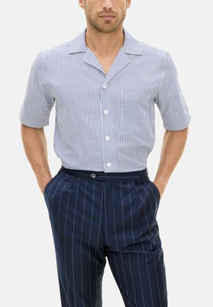 Lyhytschakko, jossa siniraitoja ja valkoista, sisällä rintatasku, yhdistettynä tummansinisiin pinstripe-housuihin, joissa on rento istuvuus ja nappisuljenta.