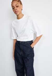 White cotton t-shirt with a round neck and short sleeves, paired with high-waisted dark blue denim pants featuring yellow stitching.