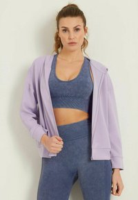 Ljuslila zip-up hoodie med avslappnad passform, kombinerad med en blå, ribbad atletisk crop top och matchande högmidjade leggings. Mjuk textur.