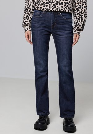 Donkerblauwe denim jeans met een rechte pijp, standaard vijf-pocket ontwerp en stevige stiksels. Gecombineerd met een patronen-langarmshirt.