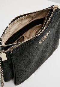 Czarna torebka kopertowa z ekoskóry o teksturowej powierzchni, złoty zamek błyskawiczny, beżowe wnętrze z wzorem logo oraz łańcuchowy pasek.