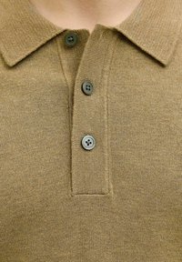 Alyvuogių žalios polo marškiniai su tekstūruotu mezginiu, turintys apykaklę ir tris mygtukus. Mygtukai apvalūs, su matinio paviršiaus apdaila.