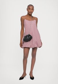 Κόκκινο και λευκό ριγέ αμάνικο φόρεμα με φαρδιά σιλουέτα. Συνδυάζεται με μια μικρή μαύρη τσάντα και μαύρα ήπια παπούτσια. Απαλή υφή υφάσματος.