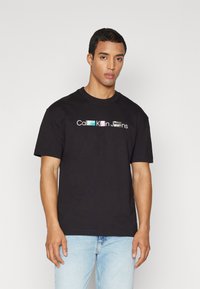 Camiseta de algodón negra con cuello redondo, mangas cortas y un logo colorido "Calvin Klein Jeans" impreso en el pecho en varios colores.