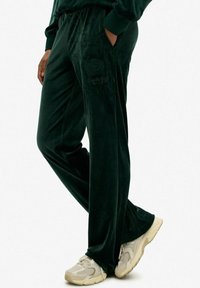 Donkergroene velours sweatpants met zijzakken en geborduurd logo. Ruime pasvorm, met een elastische tailleband. Draagt bij lichte sneakers.