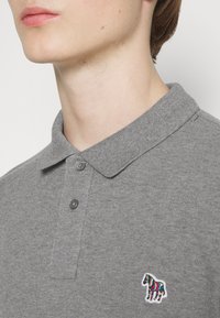 Szara koszulka polo z teksturowanej tkaniny, z kołnierzykiem, trzema guzikami oraz haftem w multikolorowego zebry na lewej piersi.