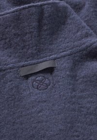 Nahaufnahme von dunkelblauem strukturiertem Stoff mit gesticktem Schlaufenmuster und gesticktem kreisförmigen Blumenmuster auf Kleidung.