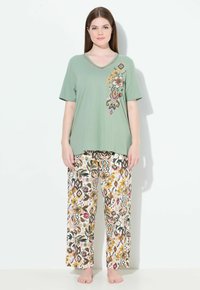 Lichtgroene korte mouwen V-hals top met bloemborduursels aan de linkerkant, gecombineerd met gebloemde beige pyjamabroek met kleurrijke bloemen en vormen.