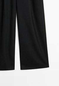 Pantalons noirs à rayures verticales avec une coupe ample. Le tissu semble lisse, avec des lignes verticales étroites et des ourlets droits. Design simple, sans quincaillerie visible.