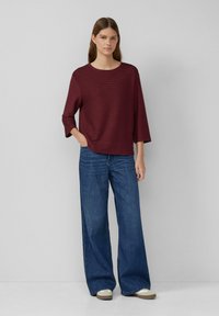 Maglioncino a righe bordeaux con maniche a tre quarti, abbinato a jeans blu a gamba larga e sneakers beige. Design semplice e vestibilità rilassata.