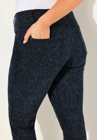 Pantalones de mezclilla azul oscuro con un sutil patrón de hojas, corte ajustado, bolsillos estándar y una cintura de altura media, con una textura suave.