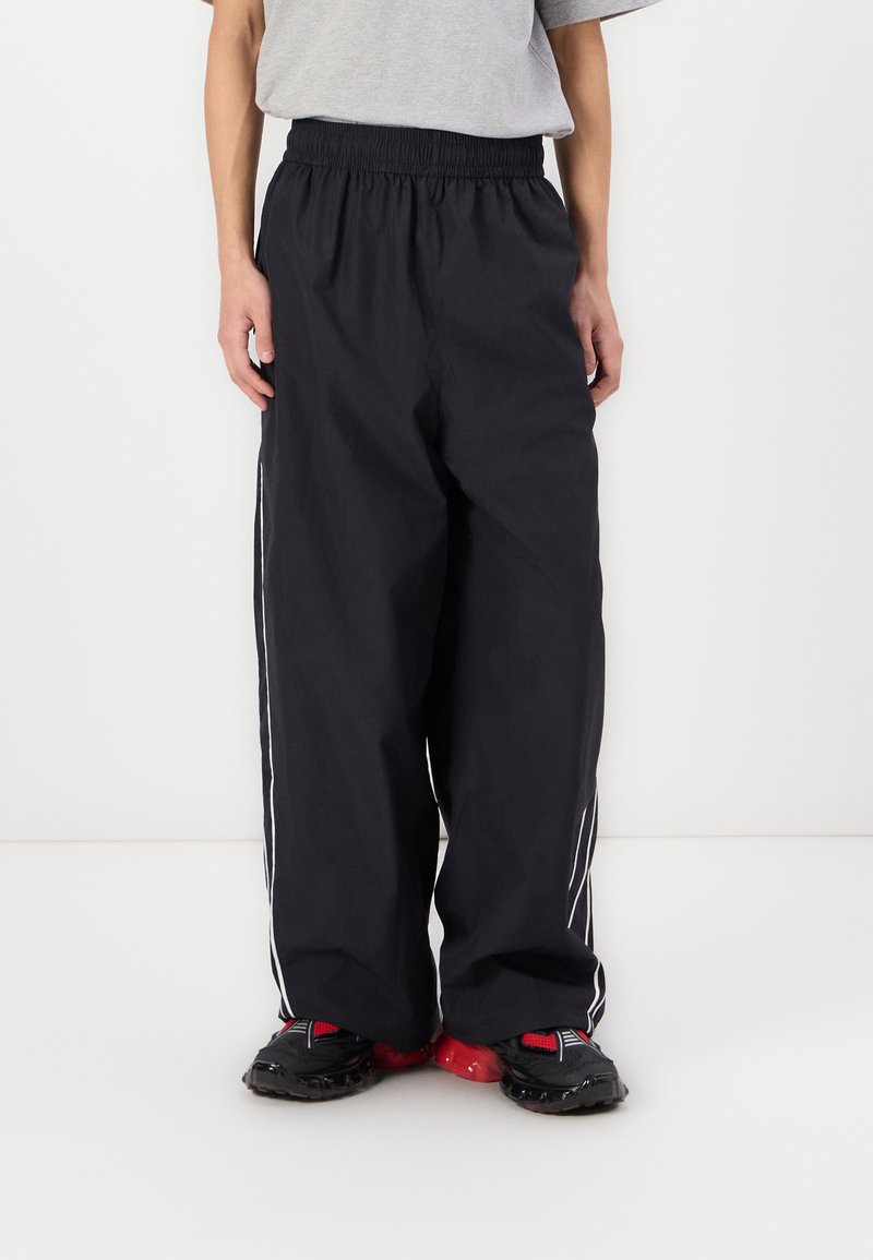 Pantaloni negri, lejeri, cu talie elastică și dungi albe pe laterale. Realizați dintr-un material ușor, cu o textură fină și un design aerodinamic.