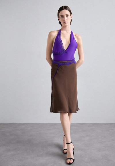 Paarse halterneck top met kantafwerking en een bruine rok met een zijsplit, gemaakt van soepel stof; gecombineerd met zwarte gespenhakschoen.