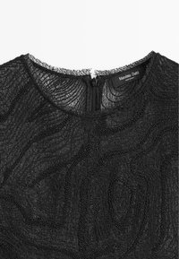 Sort tekstureret top med et bølgende mønster, prydet med små perler. Den har en rund udskæring og en lynlås bagpå.