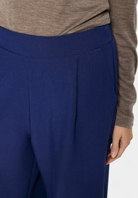 Blauwe broek met een brede tailleband, voorkleur en een gladde, zachte textuur. De stof lijkt lichtgewicht en duurzaam.
