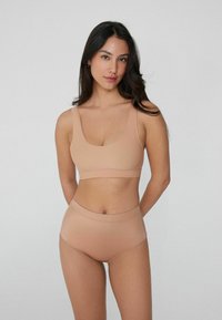 Nude bezešvé podprsenka a vysoké kalhotky, měkká textura, základní design, široké ramínka, jemný lesk, minimální detaily šití.