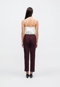 Caraco en satin vert clair à bretelles fines associé à un pantalon taille haute bordeaux. Le modèle porte des chaussures à talons noires.