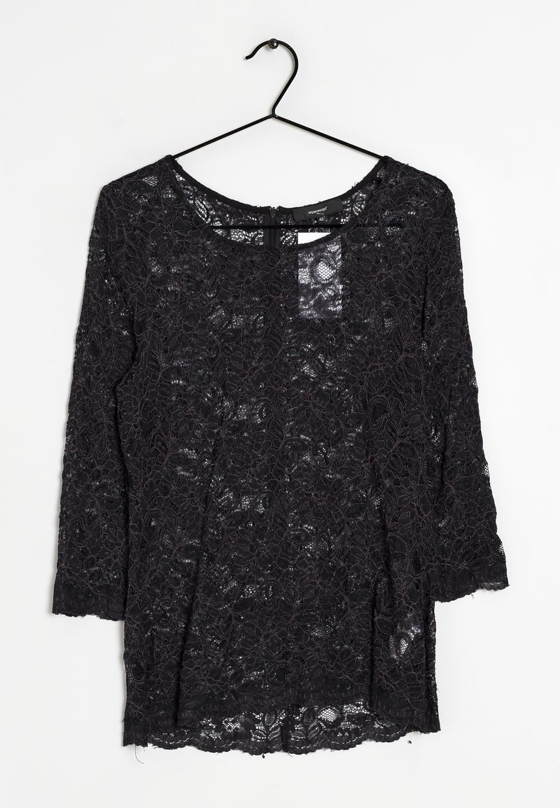 Schwarzes Spitzenoberteil mit 3/4-Ärmeln, Rundhalsausschnitt, transparenter Textur, floralen Muster und einer leichten Rundung am Saum. Hängt an einem schwarzen Haken.