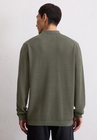 Maglione a maniche lunghe di colore verde oliva con un design a maglia testurizzata e polsini a costine, dotato di colletto classico e una vestibilità rilassata.