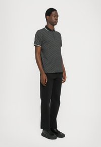 Polo noir à motifs avec manches courtes et col, associé à un jean noir et des baskets noires. Tissu texturé avec des accents contrastés.