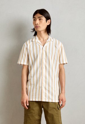 Camisa de manga corta a rayas en blanco y beige, con cuello camp y cierre de botones, confeccionada en una tela ligera, combinada con pantalones cargo en color verde oliva.