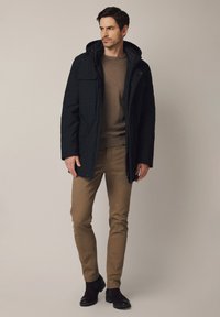 Ciemnoniebieska kurtka z kapturem z dwoma przednimi kieszeniami, brązowy sweter pod spodem, jasnobrązowe spodnie i czarne botki za kostkę. Gładki, usztywniany materiał.