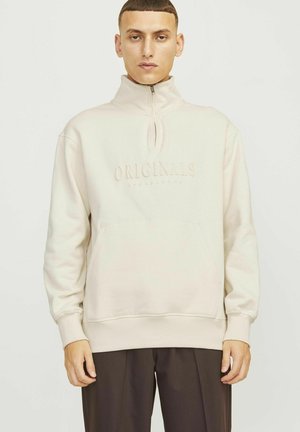 Beige Zip-Up Sweatshirt mit hohem Kragen, ausgestattet mit einer Fronttasche und geprägtem "ORIGINALS"-Logo. Hergestellt aus weichem Stoff mit glatter Textur.