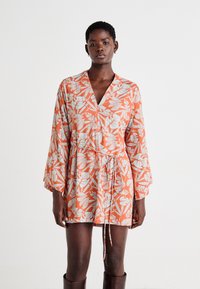 Robe florale orange avec un décolleté en V, des manches longues en forme de cloche et une taille à nouer. Présente des motifs de feuilles blanches et une texture de tissu douce.