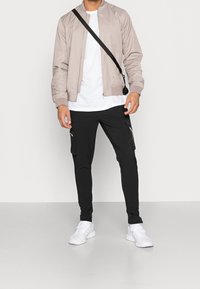 Lichtbeige bomberjack met rits, gecombineerd met zwarte cargobroeken met ritszakken en witte sneakers.