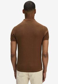 Brun kortärmad polo med ribbad textur och enhetlig färg, som har en klassisk krage och en figurnära silhuett.