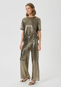 Ensemble comprenant un haut en sequins dorés et un pantalon large, offrant une coupe décontractée et des manches courtes, avec une texture lisse et une finition scintillante.