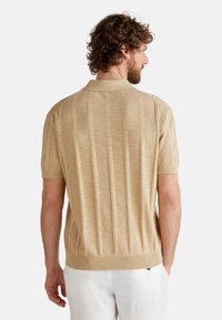 Beige polo shirt with short sleeves featuring a textured vertical stripe pattern, finished with a ribbed collar and hem.