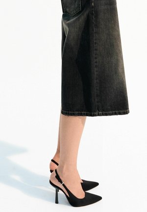 Musta, teräväkärkinen slingback-kengät, joissa on stiletto-korko. Tasainen matta pinta, avonaisella takana ja säädettävällä hihnalla. Yhdistetty tummiin farkkuhameeseen.