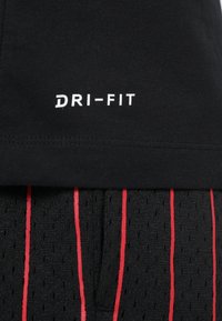 Camiseta negra DRI-FIT con una textura suave y un diseño minimalista, combinada con shorts negros transpirables que tienen rayas verticales rojas.