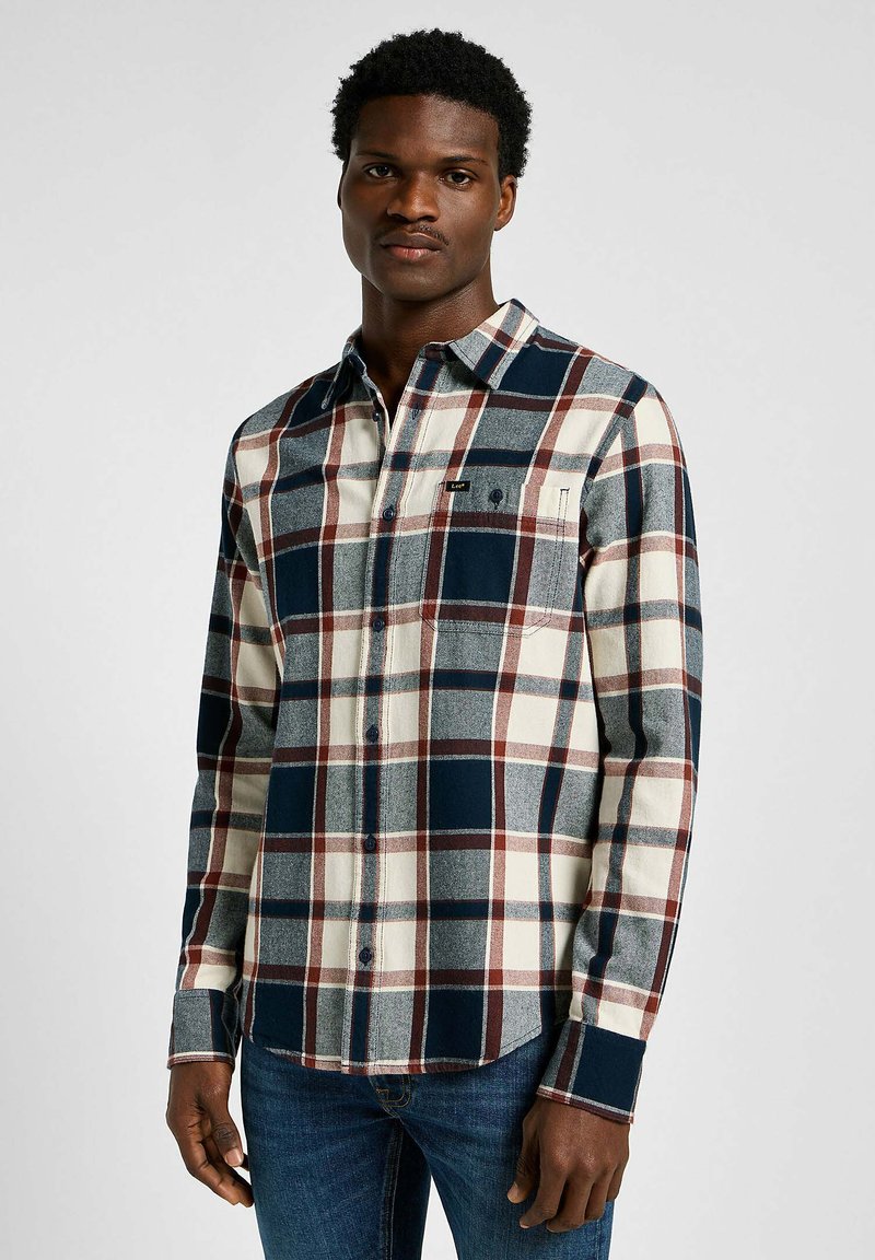 Camicia di flanella a quadri con un motivo crema, blu navy e bordeaux. Maniche lunghe, chiusura con bottoni sul davanti e taschino sul petto.