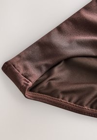 Gros plan d'un tissu marron lisse et brillant avec des coutures visibles et des bords pliés sur un fond clair.