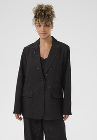 Černý blazer vyrobený z texturovaného materiálu s rozptýlenými stříbrnými akcenty, s dvěma knoflíky, výstřihy do "V" a předními kapsami.