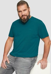 Morska bawełniana koszulka z okrągłym dekoltem. Krótkie rękawy, luźny fason i małe logo marki na piersi. Noszona z szarymi dżinsami.