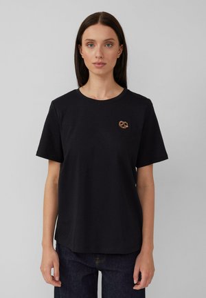 T-shirt en coton noir à manches courtes avec un petit emblème en forme de bretzel en bronze sur le côté gauche de la poitrine, avec une coupe décontractée.