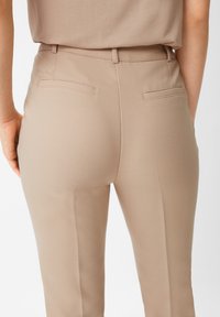 Beżowe spodnie o dopasowanym kroju z teksturowanym wykończeniem, z dwiema tylnymi kieszeniami i prostym krojem nogawek, zaprojektowane z myślą o dopasowanym wyglądzie.