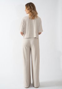 Beiger Cropped-Top mit kurzen Ärmeln, kombiniert mit weit geschnittenen Hosen. Der Stoff hat ein dezentes strukturiertes Muster. Einfarbiger Hintergrund.
