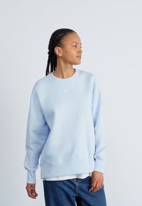 Světle modrá mikina s kulatým výstřihem a žebrovanými manžetami. Na hrudi je umístěno malé bílé logo Nike. Volný střih s hladkou strukturou.