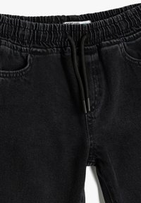 Joggers de mezclilla negra con cintura elástica y cordón ajustable. Cuenta con bolsillos laterales y un acabado suave y texturizado.