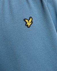 Lyseblå T-skjorte med en glatt tekstur som har en svart og gul ørnerelatert logo brodert på brystet. Enkelt design, kortermet.